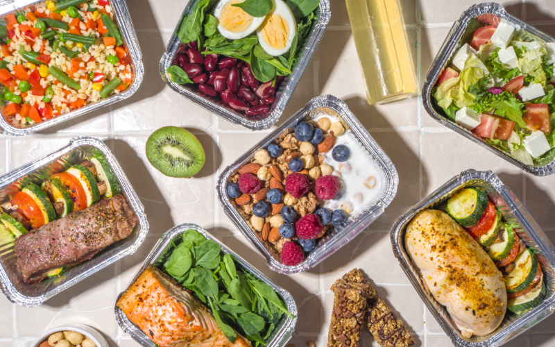Marmitas com vegetais, ovos, grãos, frutas e snacks saudáveis.