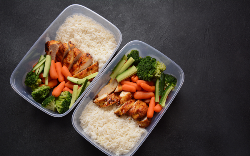 Marmitas caseiras com arroz, legumes crus e cozidos, e frango grelhado.