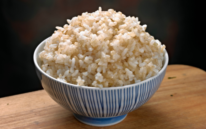 Tigela de porcelana listrada com arroz integral cozido, sobre mesa de madeira.