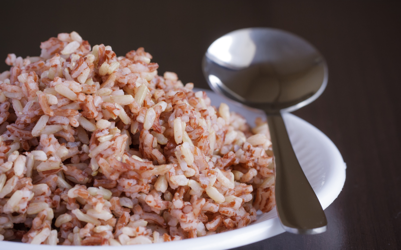 Arroz integral cozido e soltinho servido em prato branco com colher de metal.